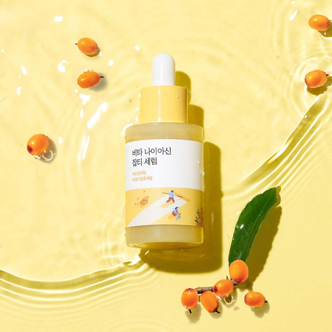 ROUND LAB Vita Niacin Spot Serum 30ml bottle on yellow surface with sea buckthorn berries and water ripples.
