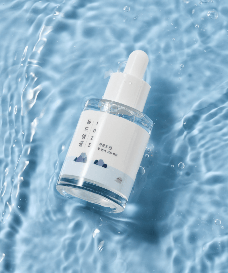 Bottle of ROUND LAB 1025 Dokdo Ampoule 45g on a water surface, showcasing skincare product design.