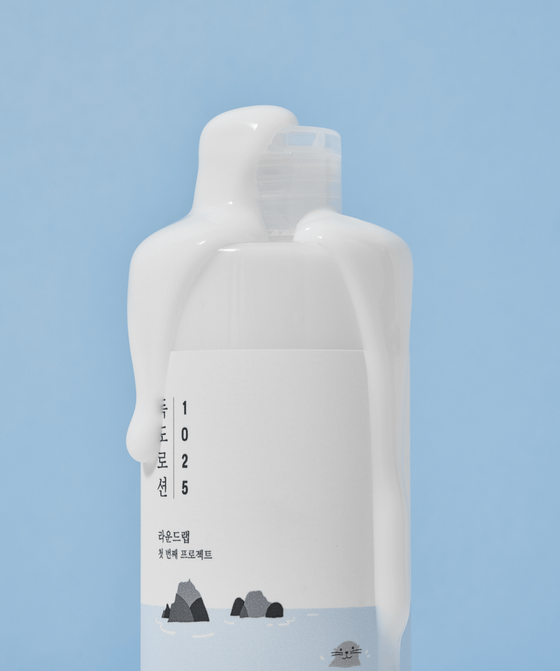 ROUND LAB 1025 Dokdo Lotion 400ml bottle with lotion dripping, against a blue background.