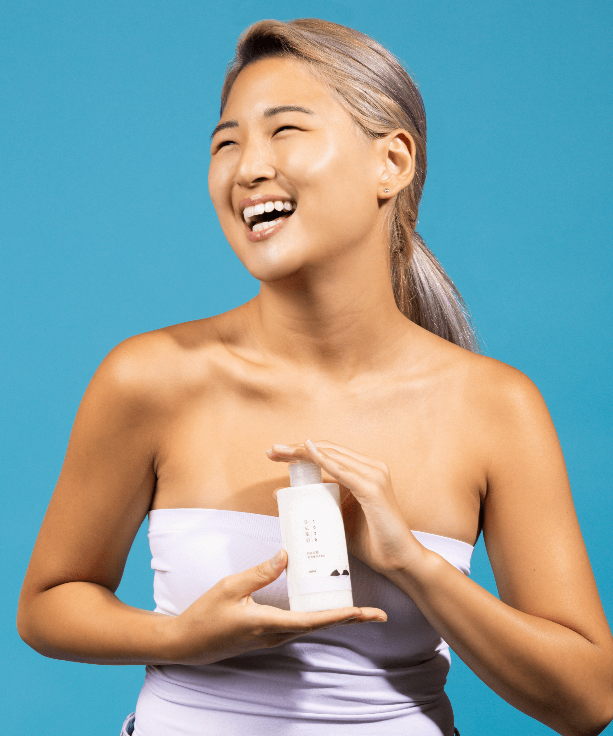 Smiling person holding ROUND LAB 1025 Dokdo Lotion 400ml against a blue background