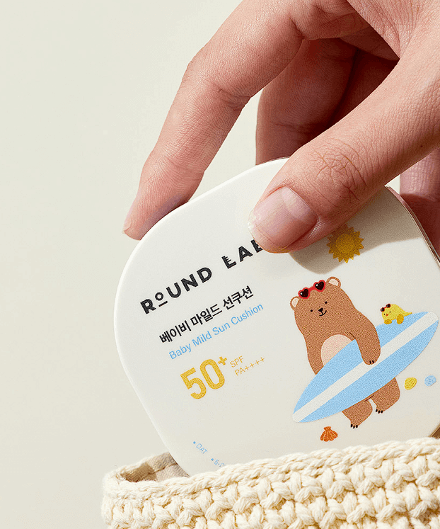 ROUND LAB Baby Mild Sun Cushion 16g in hand, SPF 50 packaging design with bear and chick illustration, eco-friendly skincare.