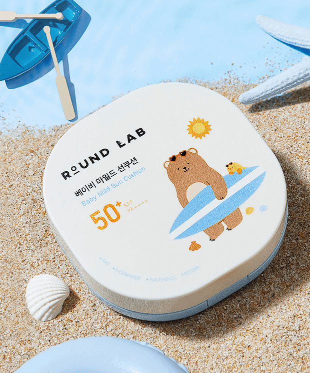 ROUND LAB Baby Mild Sun Cushion 16g on sandy beach with seashells and blue accents