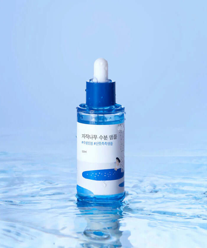 ROUND LAB Birch Moisture Ampoule 50ml bottle on water surface with blue backdrop.