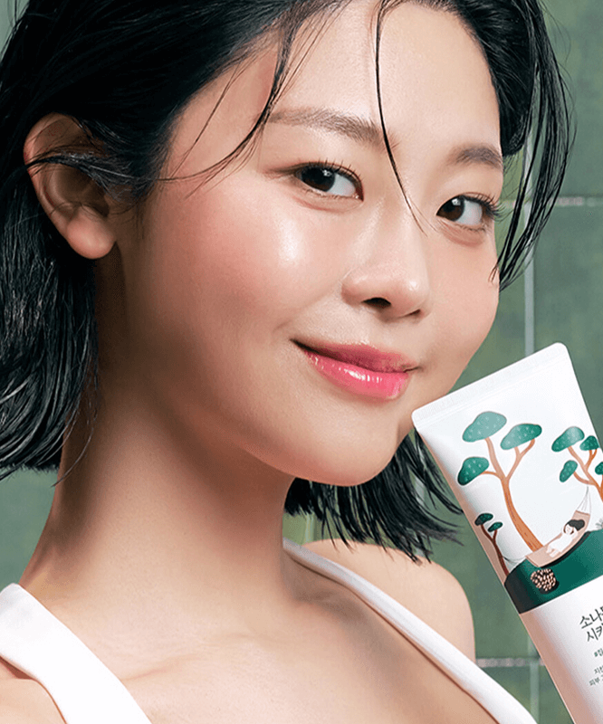 Smiling woman holding ROUND LAB Pine Calming Cica Cleanser 150ml in her hand