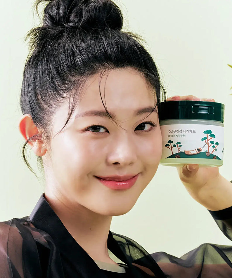 Smiling woman holding ROUND LAB Pine Calming Cica Pads 50 sheets with gentle skincare benefits.