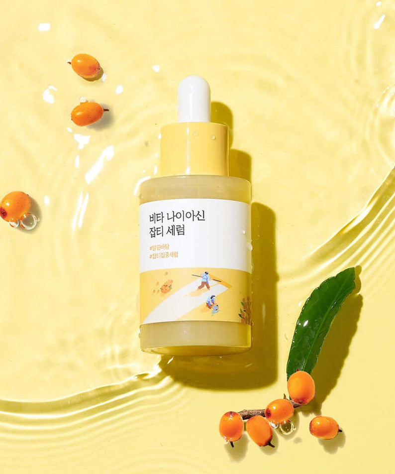 ROUND LAB Vita Niacin Spot Serum 30ml bottle on yellow surface with sea buckthorn berries and water ripples.