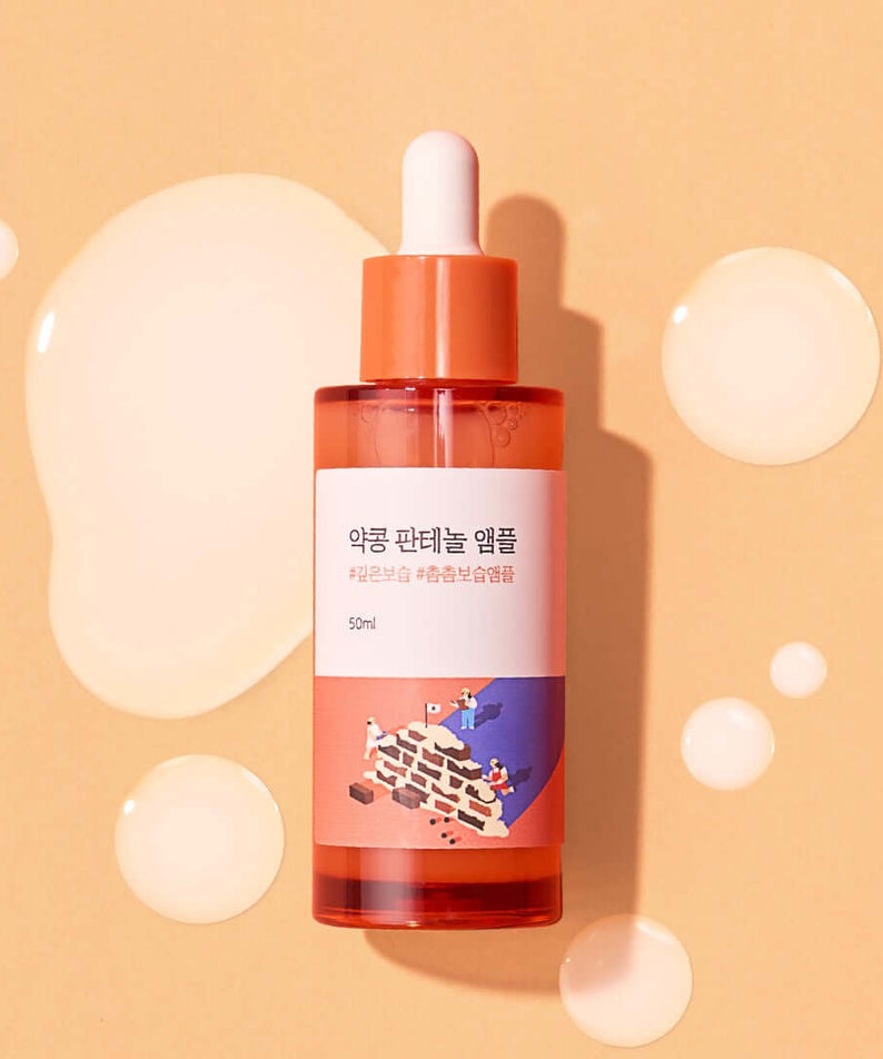 Bottle of ROUND LAB Pine Calming Cica Ampoule 30ml on peach background with liquid drops.