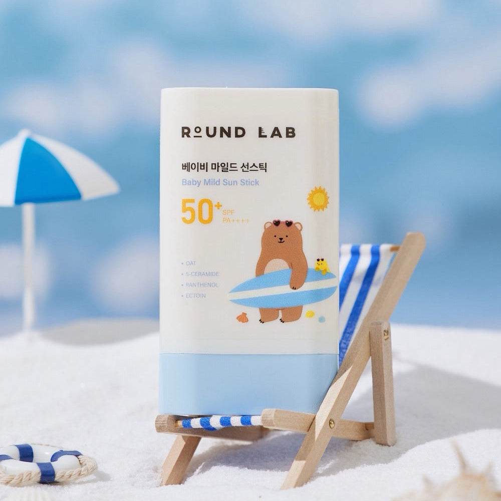 ROUND LAB Baby Mild Sun Stick SPF 50+ PA++++ 21g on a beach chair with a beach umbrella in the background