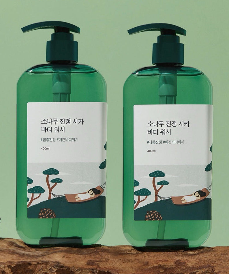 Two bottles of ROUND LAB Pine Calming Cica Body Wash 400ml with green pumps against a green background.