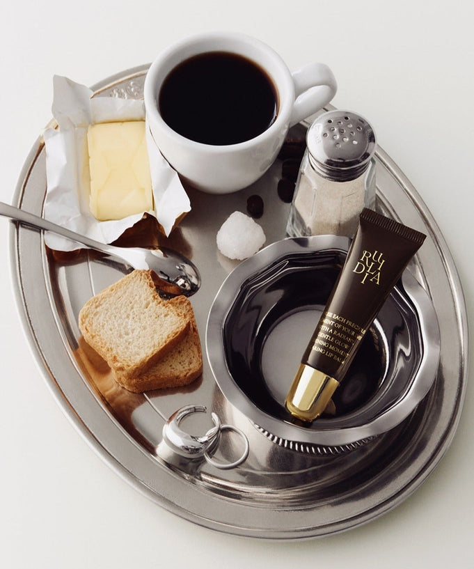 RULIDIA Shining Moment Caring Lip Balm 8g on a silver tray with coffee, toast, and butter.