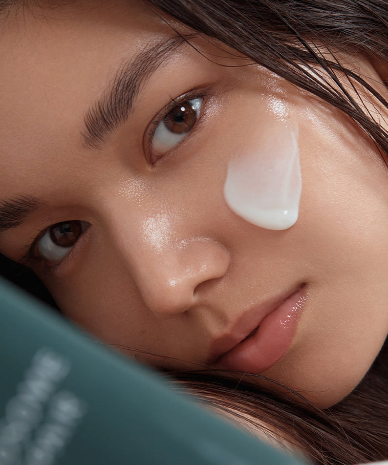 Close-up of a woman applying SHAISHAISHAI Liposome Repair Milky Cream 50ml to her cheek for skincare routine.