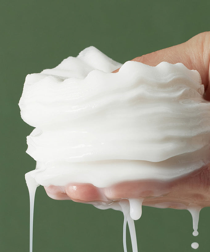 Hand holding layers of moist pads against a green background, depicting texture and consistency of SHAISHAISHAI Repair Milky Skin Peel Pad 60 Pads 120ml.