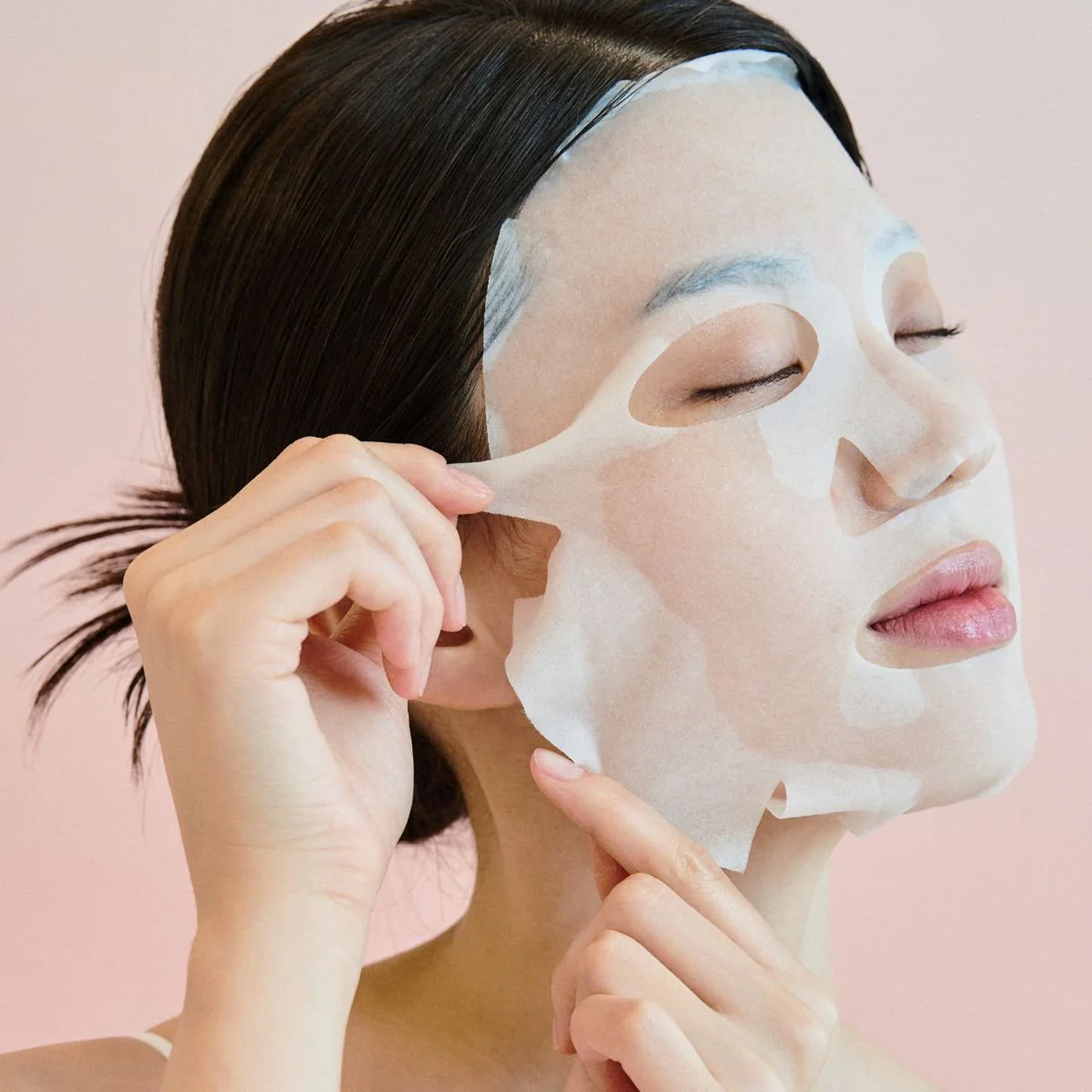 Woman applying SKIN1004 Madagascar Centella Pore-Melting Clarifying Mask 23ml [5 sheets] on a pink background.