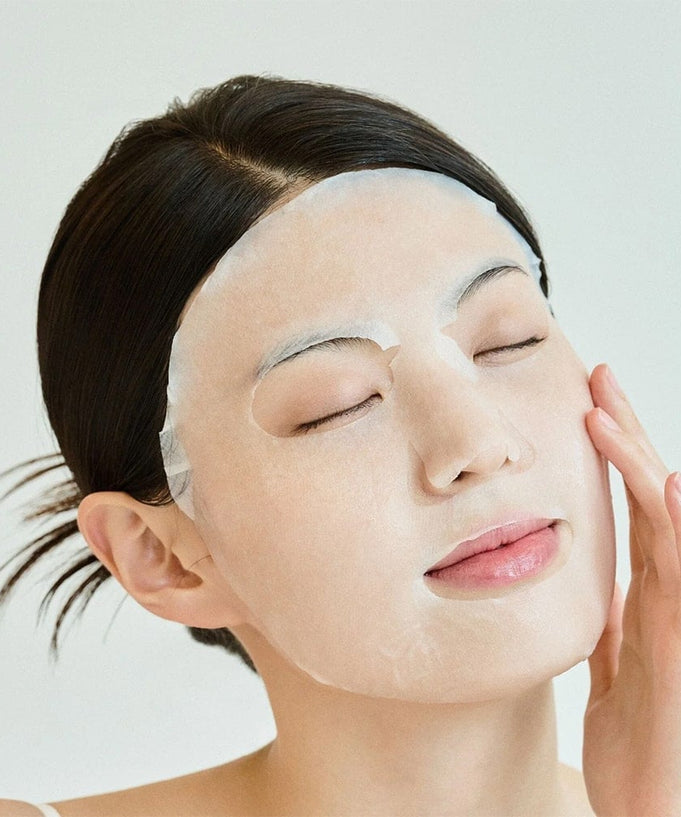 Woman using SKIN1004 Madagascar Centella Tone Brightening Glow Mask 25ml [5 sheets] for radiant skin.