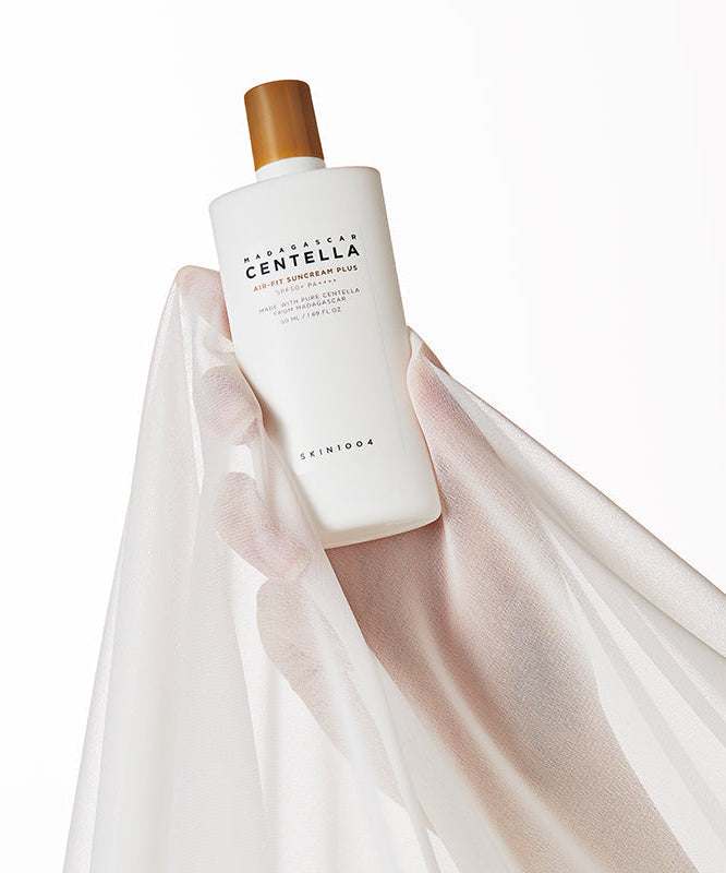 SKIN1004 Madagascar Centella Air-fit Sunscreen Plus 50ml bottle held against a sheer fabric background.