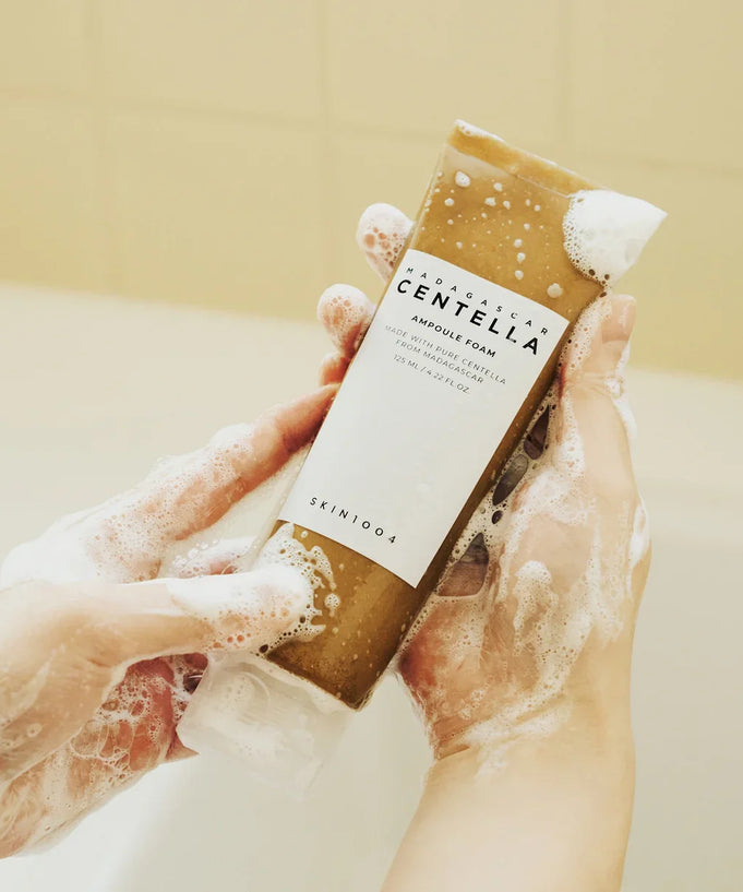 Hands holding SKIN1004 Madagascar Centella Ampoule Foam 125ml with foamy lather, showcasing the skincare product in use.