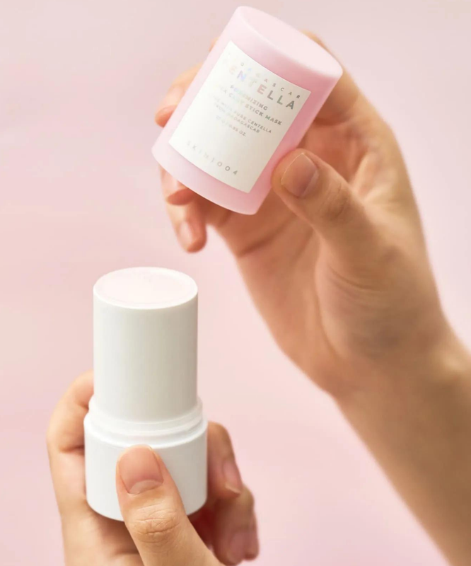 Hands holding SKIN1004 Madagascar Centella Poremising Quick Clay Stick Mask 27g with soft pink background.