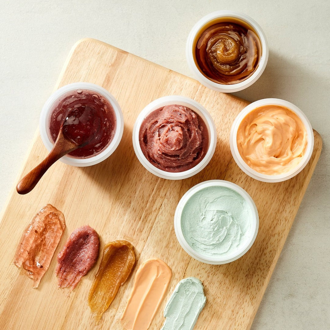 Assortment of SKINFOOD Food Mask 120g varieties displayed on a wooden board showcasing diverse textures and colors.