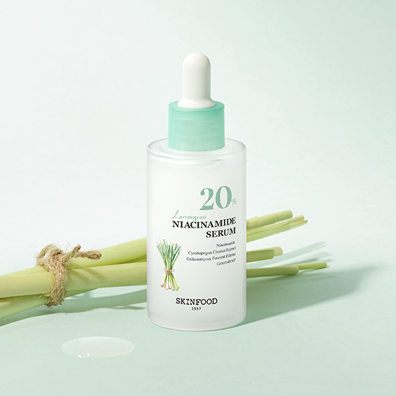 SKINFOOD Lemongrass Niacinamide 20 Serum 50ml bottle next to fresh lemongrass and serum drop on a green surface.