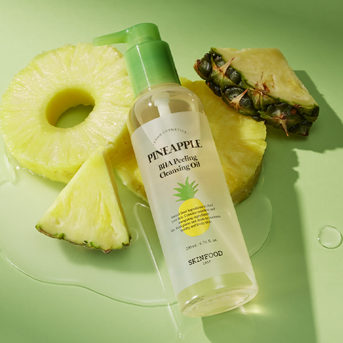 SKINFOOD Pineapple BHA Peeling Cleansing Oil 200ml bottle surrounded by fresh pineapple slices on a green background