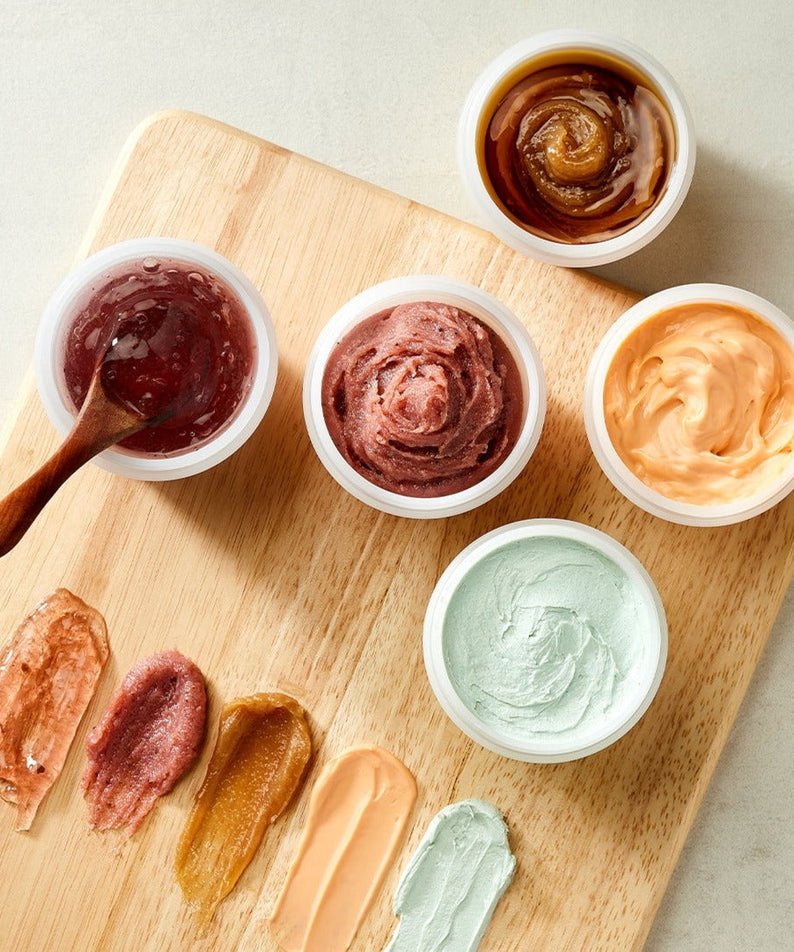 Assortment of SKINFOOD Food Mask 120g varieties displayed on a wooden board showcasing diverse textures and colors.