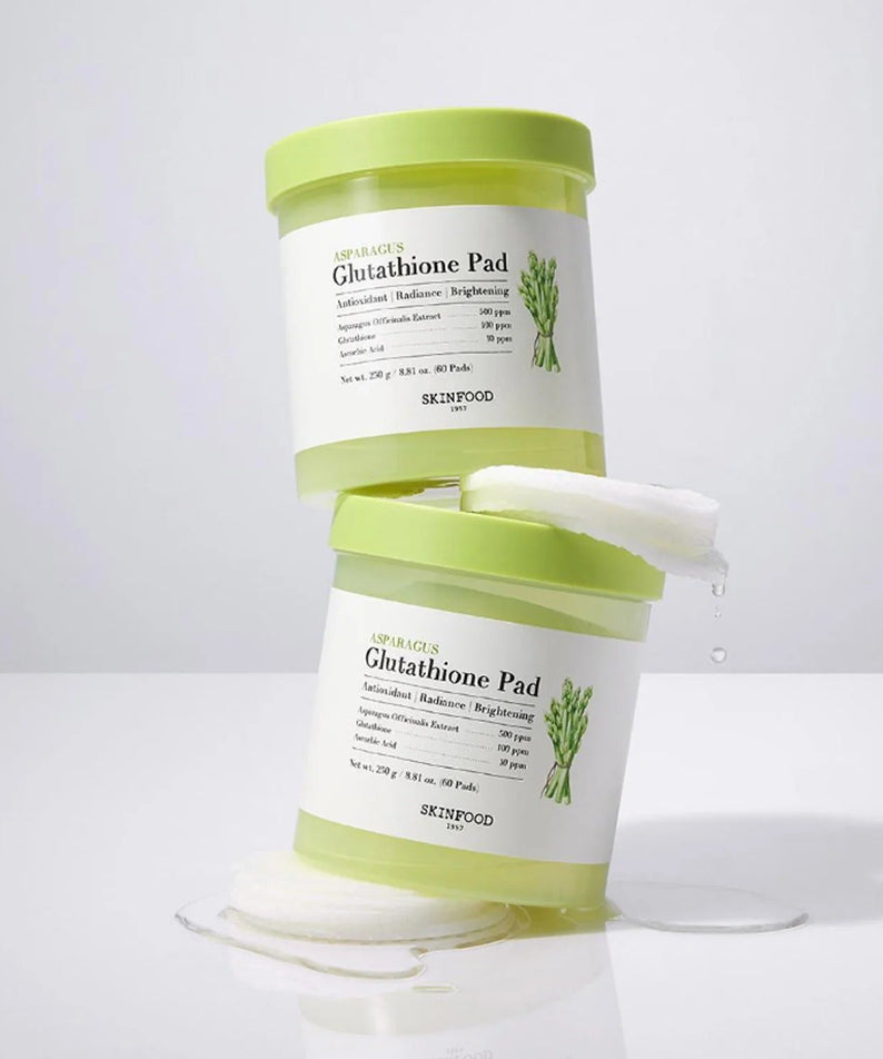 Stacked containers of SKINFOOD Asparagus Glutathione Pad (60 Pads) with pads and moisture visible, emphasizing skincare benefits.