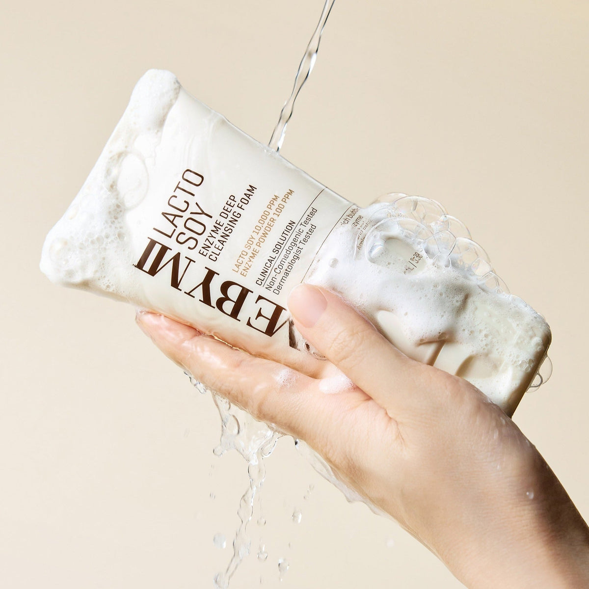Hand holding SOME BY MI Lactosoy Enzyme Deep Cleansing Foam 100ml with water and bubbles, showcasing cleansing foam texture.
