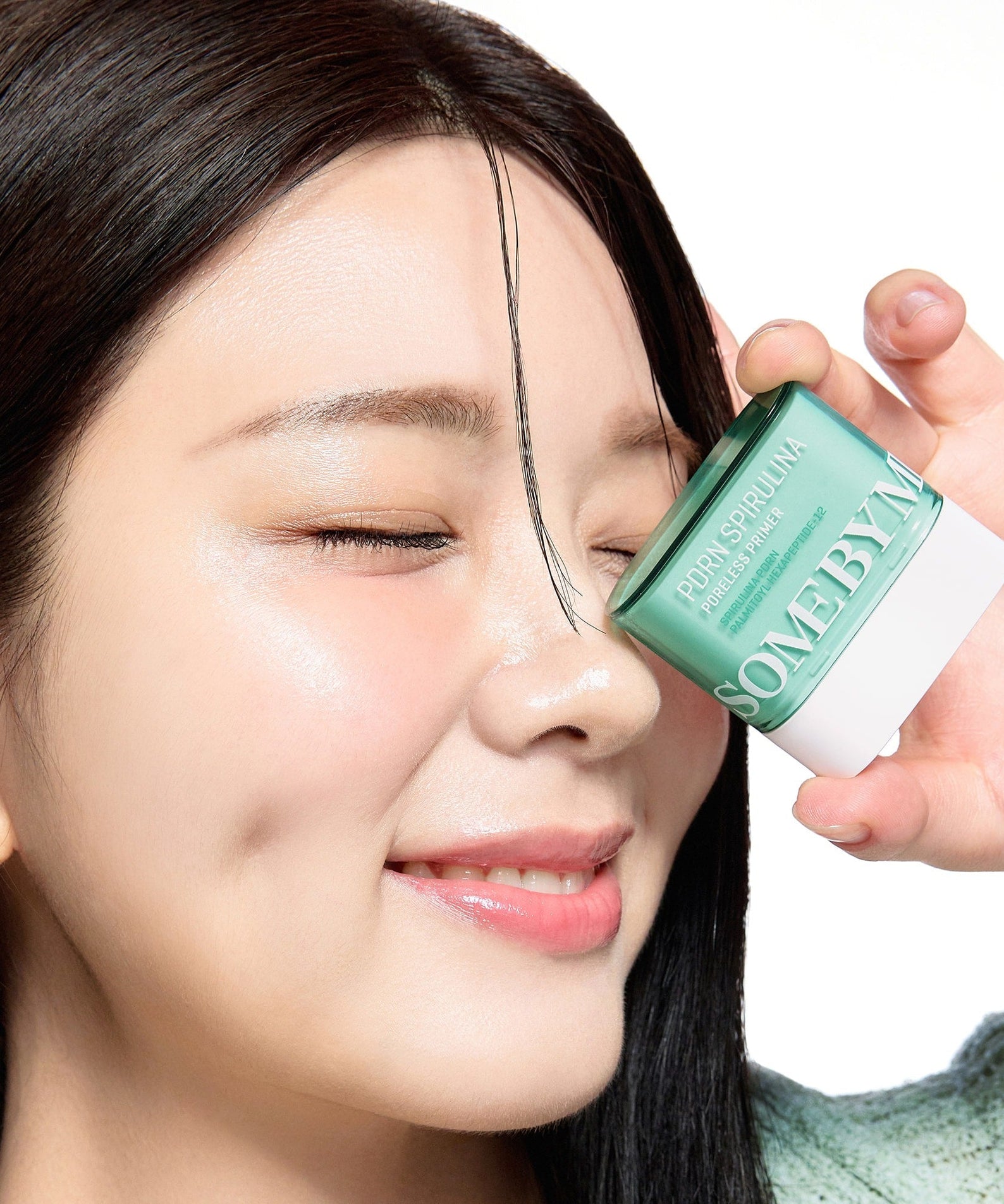 Woman holding SOME BY MI PDRN Spirulina Poreless Primer 10g next to her face, smiling with clear skin.