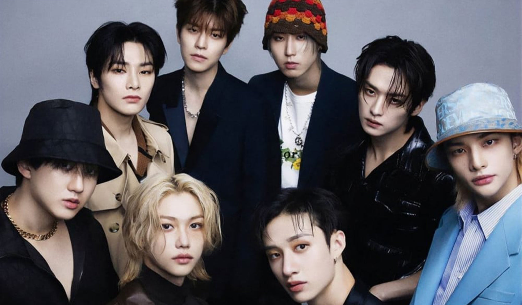 Group portrait of eight stylish individuals in fashionable outfits with hats and accessories against a neutral background.