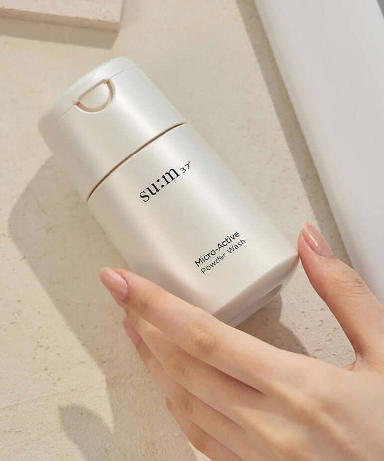Hand holding SU:M37 Microactive Powder Wash 60g bottle on light surface