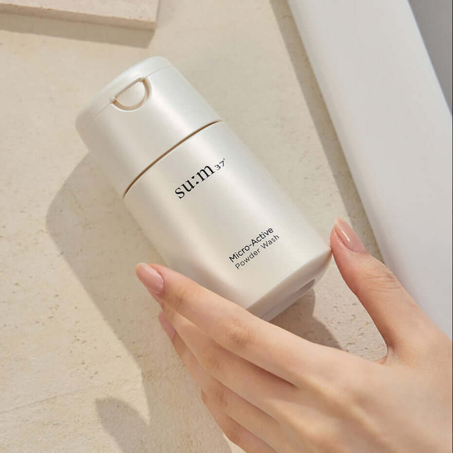 Hand holding SU:M37 Microactive Powder Wash 60g bottle on light surface