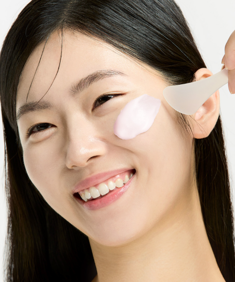 Woman applying SUNGBOON EDITOR Boosting Modeling Pack Apple Peel Glow Soothing to her face with a spatula, demonstrating skincare routine.