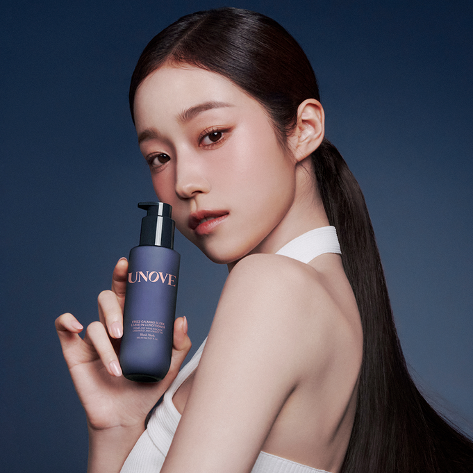 Model holding UNOVE Frizz Calming Sleek Leave-In Conditioner 150ml bottle against a dark background