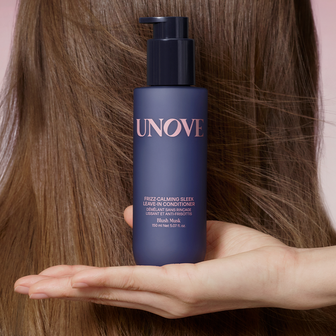 UNOVE Frizz Calming Sleek Leave-In Conditioner 150ml bottle held in hand against hair backdrop