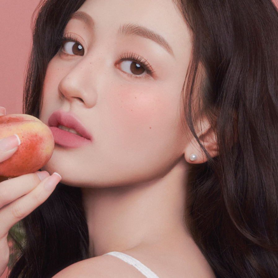 Woman holding a peach, showcasing the smooth finish of MILK TOUCH Spread Fit Blur Tint on her skin.
