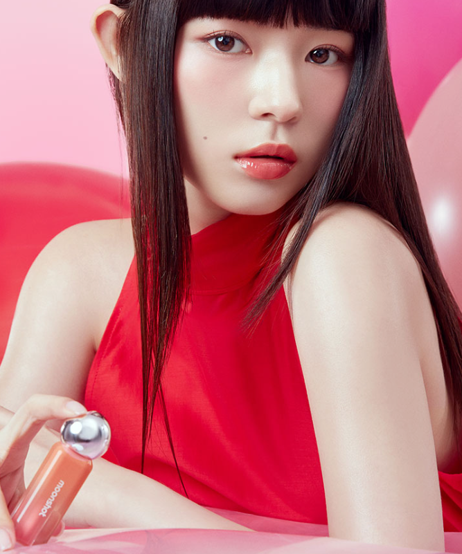 Model showcasing MOONSHOT Jelly Moon Glow Tint in a vibrant red setting, highlighting the product's glossy finish.