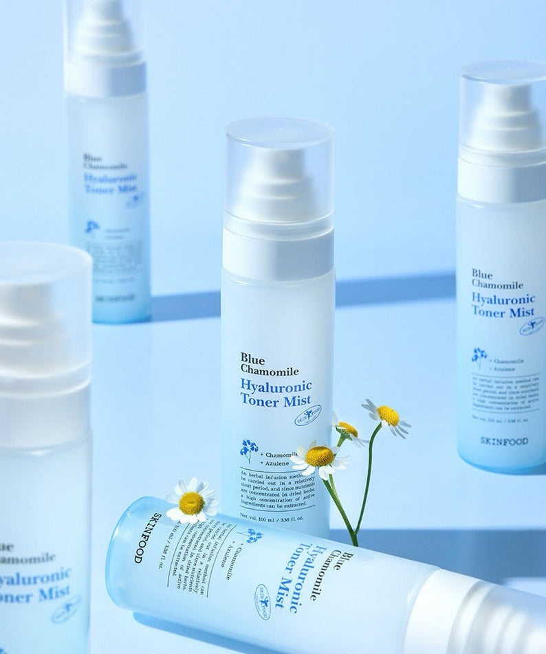 SKINFOOD Blue Chamomile Hyaluronic Toner Mist 100ml bottles arranged on a blue background with chamomile flowers.