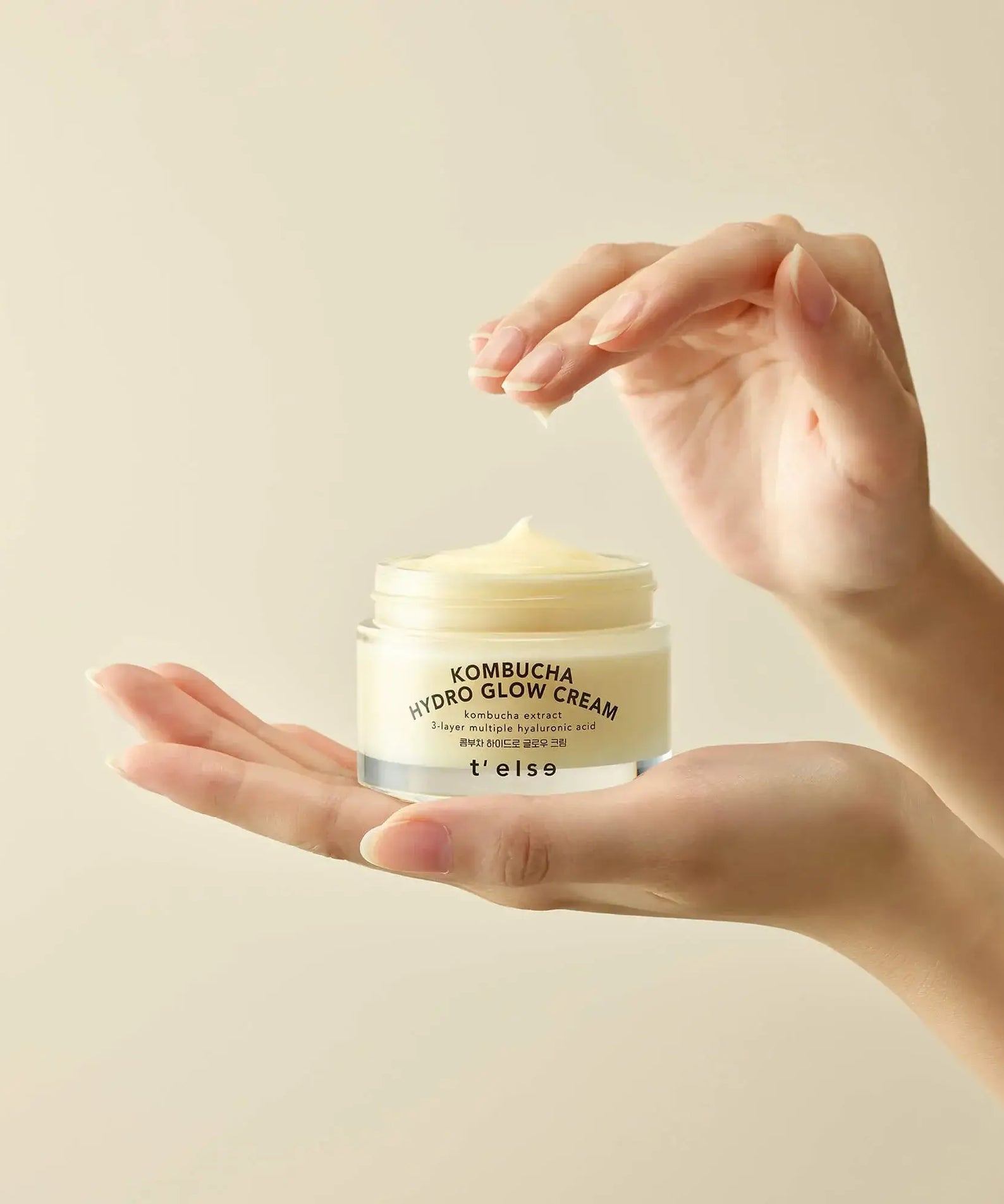 Hands holding T'ELSE Kombucha Hydro Glow Cream 50ml jar against a neutral background
