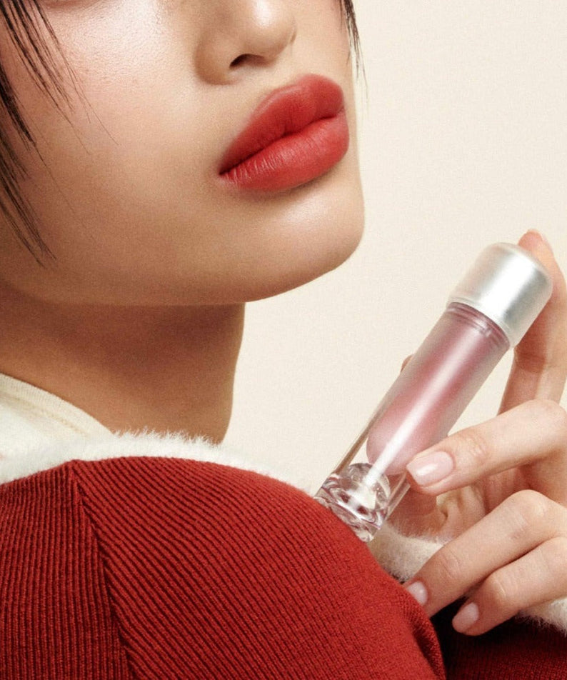 Woman holding TENSE Day Moment Cream Velvet Tint close to her lips, showcasing product texture and design.