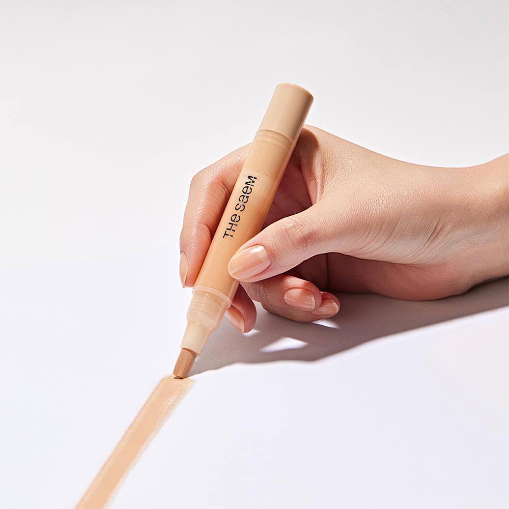 Hand holding THE SAEM Cover Perfection Pen Concealer applying product on white surface