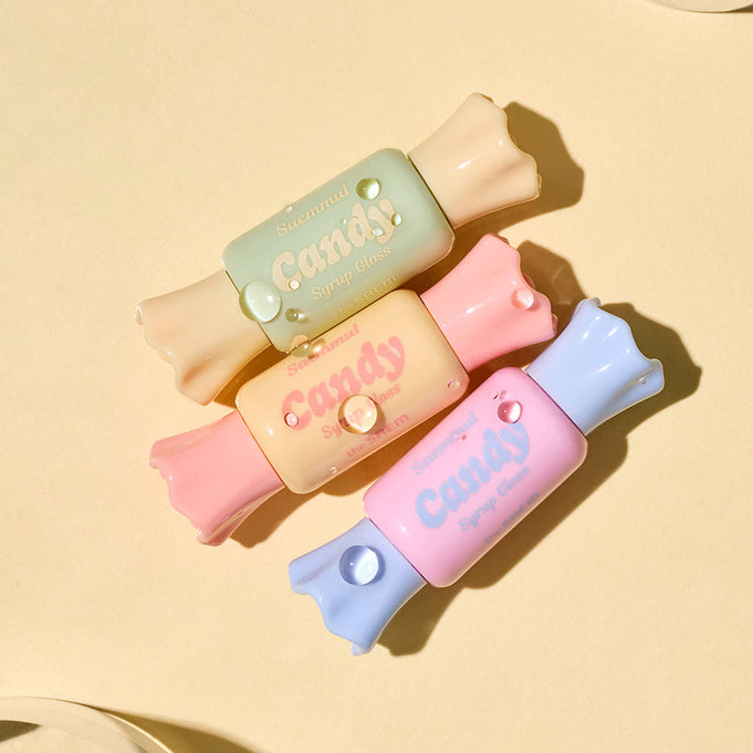 Colorful packs of THE SAEM Saemmul Candy Syrup Gloss arranged on a beige background.