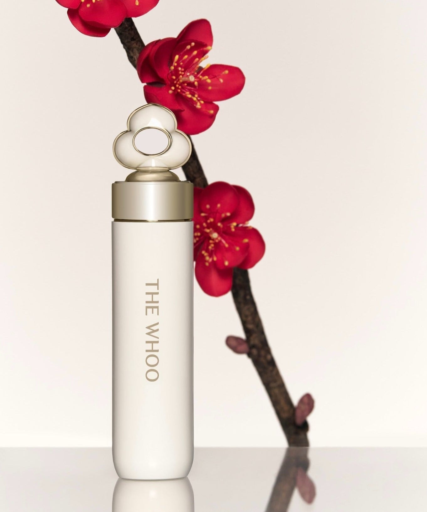 Elegant packaging of THE WHOO Essentail Lip Glow Balm with red flowers in background.