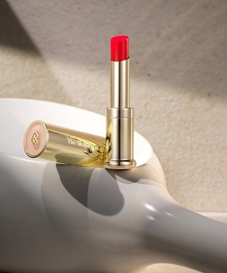 THE WHOO Gong Jin Hyang Mi Glow Lip Balm 3.3g in a sleek gold case on a reflective surface