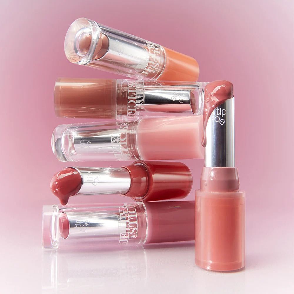 Assorted shades of TIP TOE Jelly Stick Plan lipsticks against a pink background.