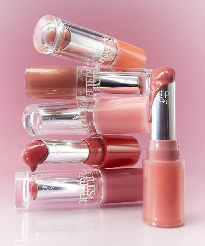 Assorted shades of TIP TOE Jelly Stick Plan lipsticks against a pink background.