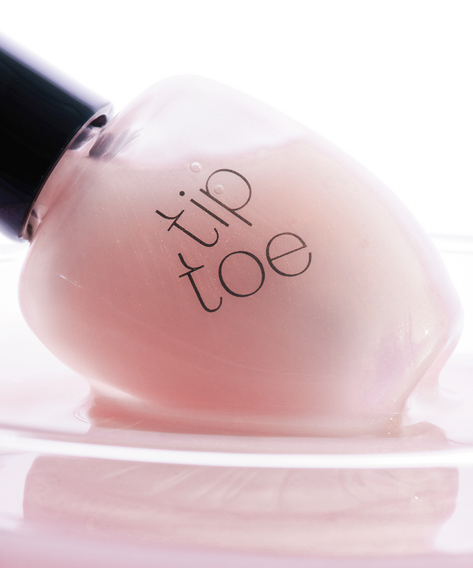 TIP TOE Sheer Topcoat Nail Polish bottle close-up on a light background.