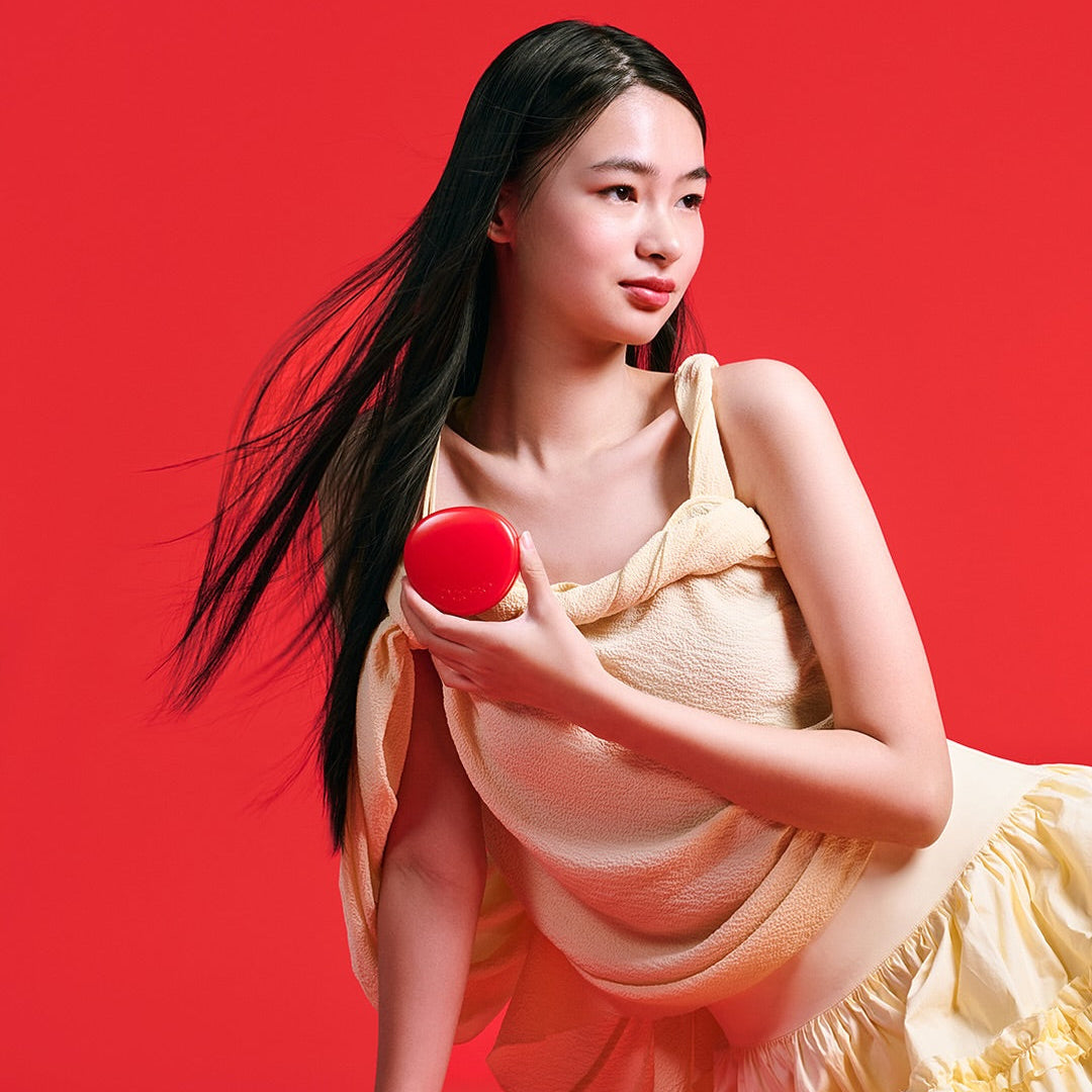 Person holding TOCOBO Apple Dewy Fit Cushion in red packaging against a vibrant red background