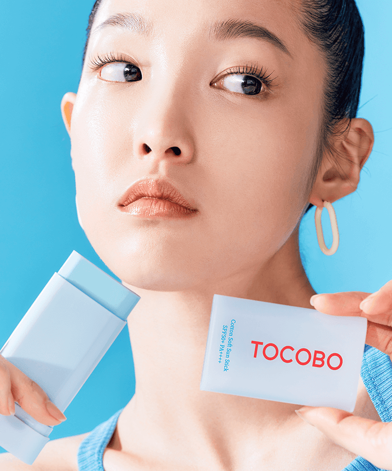 Woman holding TOCOBO Cotton Soft Sun Stick against a blue background.