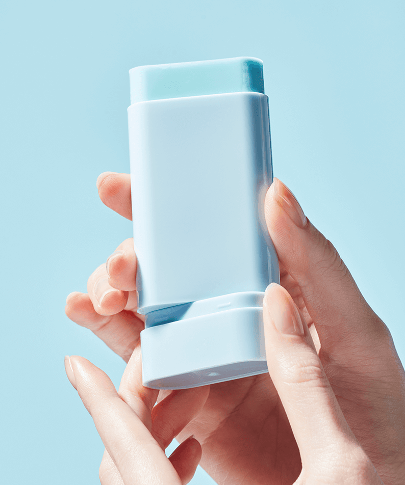 Close-up of TOCOBO Cotton Soft Sun Stick held in hands with a blue background, showcasing its sleek design and portable size.
