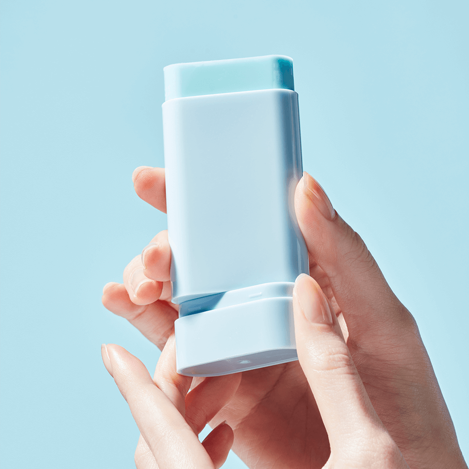 Close-up of TOCOBO Cotton Soft Sun Stick held in hands with a blue background, showcasing its sleek design and portable size.